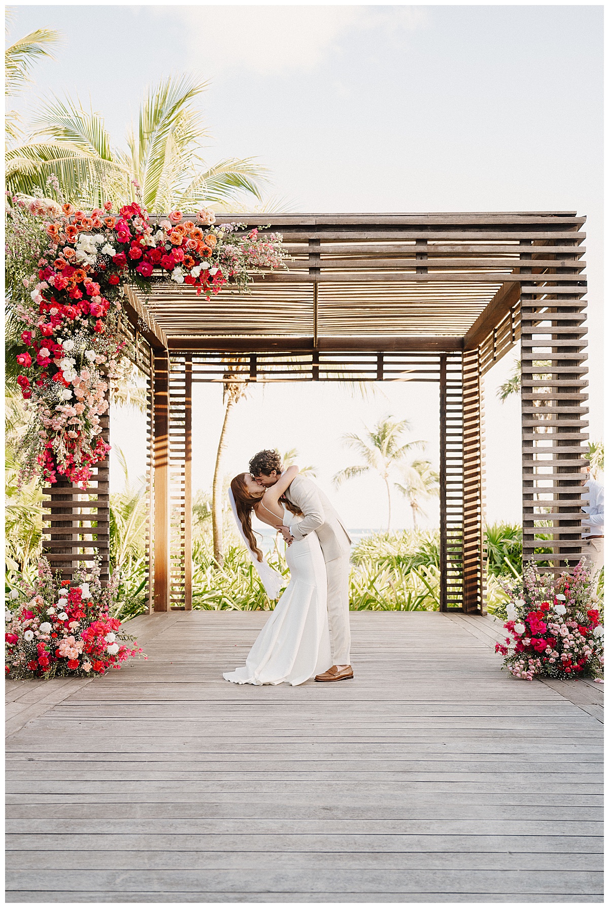 bride and groom first kiss on the beach with bright pink flowers